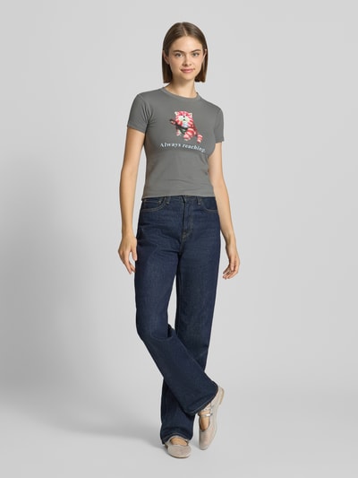 Kobiece modelka nosi Slim Fit T-Shirt mit Motiv-Print od DAISY STREET, mieszanka bawełny, okrągły dekolt, z krótkim rękawem, długość tyłu w rozmiarze S: 46 cm, szara koszulka z różowym nadrukiem z motywem, ciemnoniebieskie spodnie, całkowity widok z przodu.