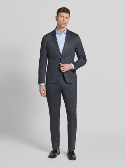 Męski model nosi Regular Fit Anzugsakko mit Viskose-Anteil von s.Oliver BLACK LABEL z nadrukiem allover, długi rękaw, kolor grafitowy, krój regular fit, klapy z kołnierzem, zapięcie na dwa guziki, kieszeń na piersi, kieszenie zewnętrzne i wewnętrzna. Ganzkörperansicht von vorne.
