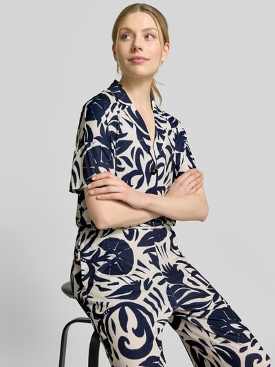 Vrouwenmodel draagt Jumpsuit met floralem allover-print van Oui in donkerblauw-crèmekleur, elastische materiaalmix, getailleerde pasvorm, reverskraag, met korte mouwen, knoopsluiting, zichtbare all-over bloemenprintstructuur, detailopname bovenlichaam