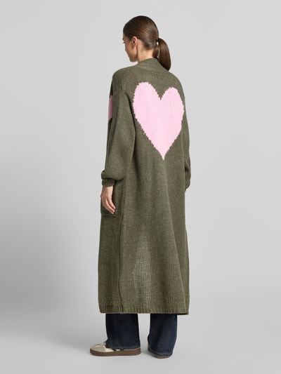 Frauenmodel trägt Strickjacke mit Woll-Anteil von miss goodlife, olivgrün mit rosa Herz-Motiv, lockerer Schnitt, Rückenansicht, Ganzkörperansicht von hinten.