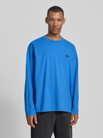 Männermodel trägt Longsleeve mit Logo-Print Modell 'GIXY' von American Vintage, leuchtend blau, Reine Baumwolle, Loose-Fit, Rundhalsausschnitt, Ganzkörperansicht von vorne.