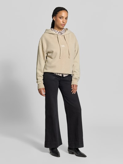 Frauenmodel trägt Oversized Hoodie aus reiner Baumwolle von Lala Berlin in Beige mit Kapuze, Label-Print, gerippten Abschlüssen, Ganzkörperansicht von vorne.