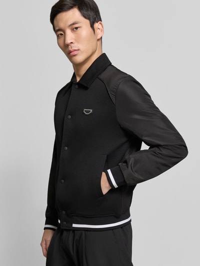 Männermodel trägt Jacke mit Label-Detail von Antony Morato in Schwarz mit Kentkragen, Druckknopfleiste, gestreiften Bündchen, Nahaufnahme Oberkörper.