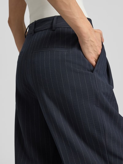 Kobiece modelka ma na sobie Hose mit Streifenmuster und Bügelfalten od Jake*s Collection, mieszanka materiałów z dodatkiem wiskozy, krój relaxed fit, wzór w paski, kanty, detal tylnej kieszeni, ciemny granat z jasnymi paskami, długość wewnętrzna nogawki 73 cm, szerokość w rozmiarze 36: 38 cm, zbliżenie na biodra i kieszeń, detal tylnej perspektywy