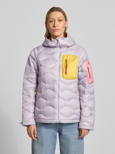 Modelka kobieca nosi kurtkę Jacke mit Entendaunen-Füllung und Kapuze od PEAK PERFORMANCE, kolory pastelowy fiolet, żółty, róż, prosty krój, wyhaftowane logo, kieszenie zapinane na zamek błyskawiczny, kaptur z troczkami, długość tyłu w rozmiarze S: 65 cm, szerokość ramion w rozmiarze S: 40 cm, szerokość w rozmiarze S: 51 cm, długość rękawów w rozmiarze S: 63 cm, wypełnienie kaczym puchem, widok całofigurowy z przodu.