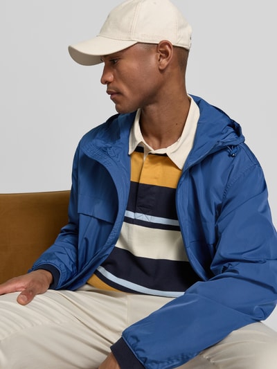 Männermodel trägt Regular Fit Regenjacke mit Logo-Stitching von Polo Ralph Lauren, look: effen, pasvorm: regular fit, capuchon met tunnelkoord, tweewegritssluiting, gestikt logo, lange mouw met elastisch mouwboord, rompzoom met tunnelkoord, zij-steekzakken. Nahaufnahme Oberkörper.