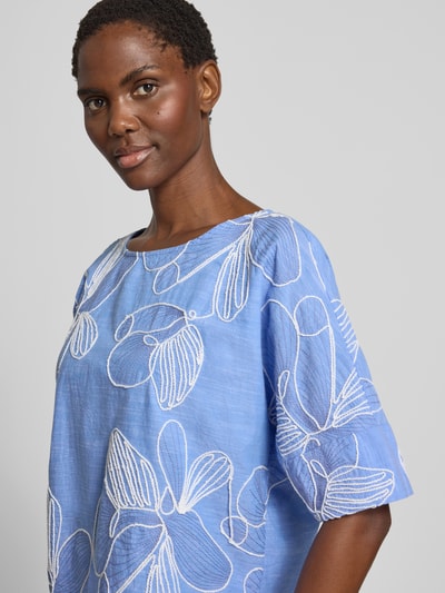 Kobiece modelka nosi Blusenshirt aus reiner Baumwolle von Christian Berg Woman, niebieski kolor, wzór na całej powierzchni, hafty, okrągły dekolt, krój regular fit, długość tyłu w rozmiarze 36: 55 cm, długość rękawów w rozmiarze 36: 29 cm, bluzka z krótkim rękawem, zbliżenie na górną część ciała.