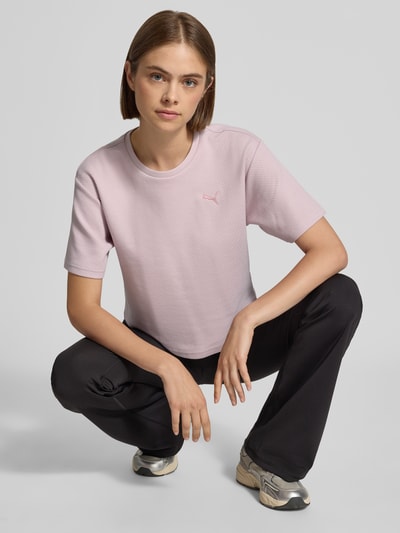 Frauenmodel trägt Relaxed Fit T-Shirt aus Häkelspitze von PUMA in zartem Rosa zu schwarzer Hose, Ganzkörperansicht von vorne, Damen T-Shirt von PUMA.