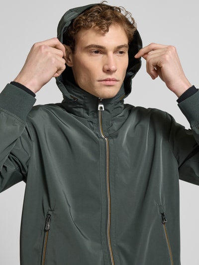 Männermodel trägt Regular Fit Jacke mit Kapuze Modell 'Como' von NAUTGÅRD in Dunkelgrün mit Reißverschlusstaschen, Nahaufnahme Oberkörper. Rückenlänge 67 cm, Schulterbreite 48 cm, Brustweite 60 cm, Ärmellänge 67 cm.