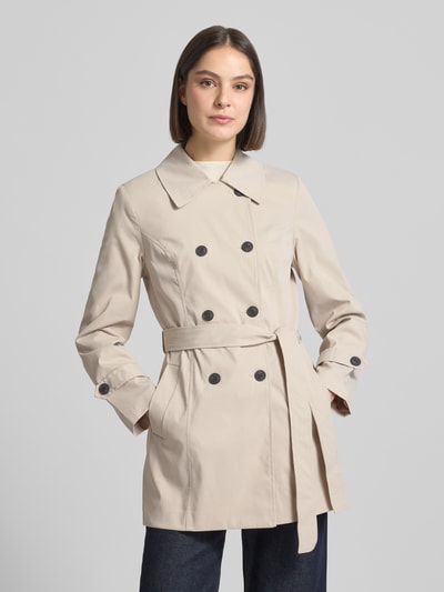 Modelka nosi trencz Regular Fit Trenchcoat mit Taillengürtel zum Binden Modell 'CHALSEA OLIVIA' von Vero Moda, efekt: jednolity kolor, wykładany kołnierz, listwa guzikowa 2-rzędowa, długi rękaw z patkami przy mankietach, wpuszczane kieszenie, wykończenie materiału: splot twill, kolor beżowy, krój regular fit. Ganzkörperansicht z przodu.