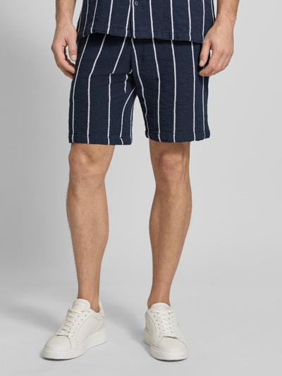 Mężczyzna nosi Shorts mit elastischem Bund und Tunnelzug von MCNEAL, bawełna, krój regular fit, szerokość w rozmiarze M 42 cm, długość nogawki 20 cm, ciemnogranatowe z białymi paskami, faktura lekko marszczona, widok z przodu na całe ciało.