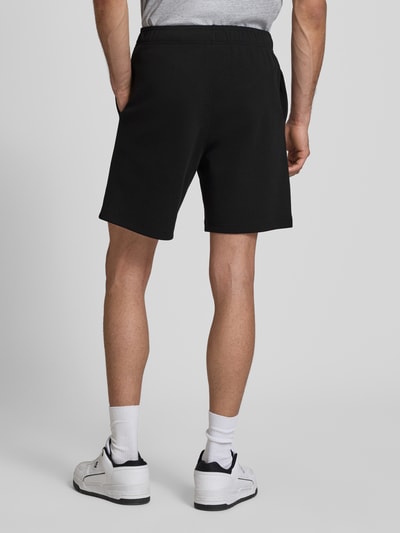 Männermodel trägt schwarze Shorts mit elastischem Bund und Label-Stitching von CHAMPION, Baumwoll-Mix, Ganzkörperansicht Rückansicht.