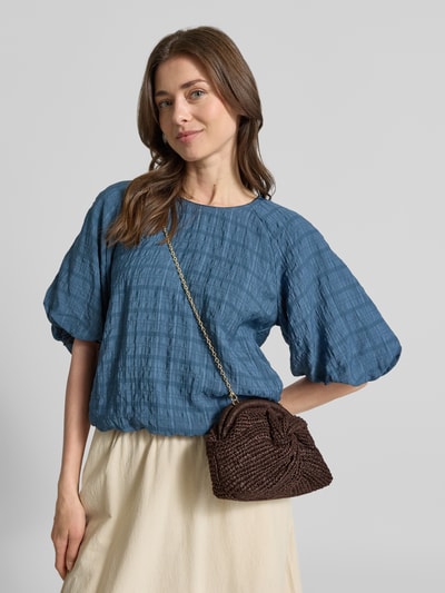 Frauenmodel trägt Handbag in Flecht-Optik Modell 'Sita' von Mango in Dunkelbraun mit Ketten-Optik, Nahaufnahme Oberkörper. Das offene Hauptfach, der abnehmbare Trageriemen und die kompakten Maße von 23x15x8 cm unterstreichen den modernen Look und machen das Accessoire vielseitig kombinierbar.