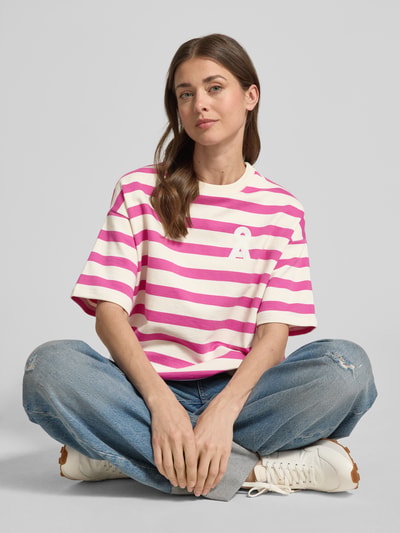 Frauenmodel trägt Oversized Fit Sweatshirt aus reiner Bio-Baumwolle Modell 'BAMIKAA' von Armedangels, pink-weiße Streifen, kurzes Logo-Stitching, Rundhals, kurzarm, Sweat-Material, Allover-Muster, Ganzkörperansicht von vorne.