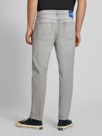 Männermodel trägt Tapered Straight Fit Jeans aus Baumwoll-Mix Modell 'BRODY' von HUGO Blue in grauer Denimoptik, Ganzkörperansicht Rückansicht.