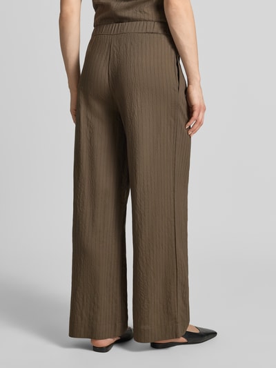 Frauenmodel trägt Stoffhose aus Viskose-Mix Modell 'TATU' von Mango, braun, Wide Leg, elastischer Bund, strukturierte Oberfläche, Ganzkörperansicht Rückansicht.