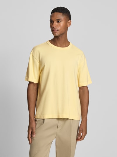 Männermodel trägt Cropped T-Shirt mit Rundhalsausschnitt von GAP in Gelb, reine Baumwolle, lockerer Schnitt, Ganzkörperansicht von vorne.