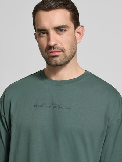 Männermodel trägt Boxy Fit T-Shirt mit Rundhalsausschnitt von HALO in Grün, Herren T-Shirt aus Reine Baumwolle, Nahaufnahme Oberkörper.