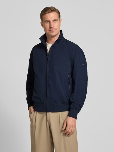 Männermodel trägt Relaxed Fit Blouson aus wasserabweisendem Material Modell 'OPENS' von BOSS Orange, Optik: Unifarben, Zweiwege-Reißverschluss, Stehkragen, Label-Patch, seitliche Eingrifftaschen, Langarm, Ärmelabschluss und Rumpfabschluss: gerippt, Nahaufnahme Oberkörper.