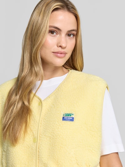 Frauenmodel trägt Relaxed Fit Weste aus Teddyfell Modell 'Hoktown' von American Vintage mit Logo-Patch, gelb, Nahaufnahme Oberkörper. Damen Weste von American Vintage, Knopfleiste, weiche Textur, strukturierte Oberfläche.