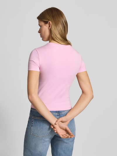 Vrouwenmodel draagt T-Shirt met Logo und Rundhalsausschnitt van Guess Jeans in lichtroze, slim fit, katoen-elastaan, rugaanzicht.