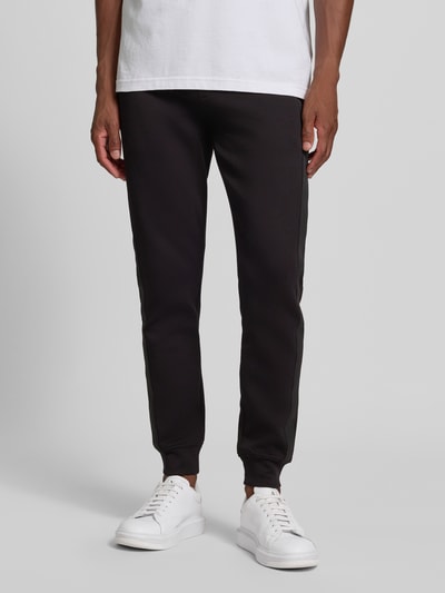 Männermodel trägt Sweatpants mit Bordüre von Armani Exchange in Schwarz, gerader Schnitt, mit Label-Print, Ganzkörperansicht von vorne.