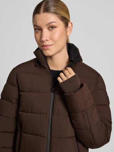 Frauenmodel trägt Jacke mit Daumenloch und Kapuze von NAUTGÅRD in Dunkelbraun, glatte Struktur, seitliche Reißverschlusstaschen, Nahaufnahme Oberkörper. Rückenlänge 58 cm, Schulterbreite 40 cm, Brustweite 48 cm, Ärmellänge 65 cm.