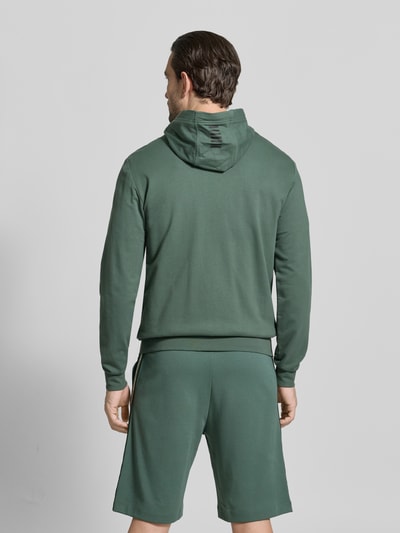 Männermodel trägt Slim Fit Sweatjacke mit Kapuze von EA7 Emporio Armani aus elastischem Baumwoll-Mix in Grün, Rückenansicht.