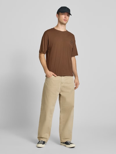 Männermodel trägt Relaxed Fit T-Shirt aus reiner Baumwolle Modell "DYLAN" von JACK & JONES in Braun, Rundhals, Print-Detail, Ganzkörperansicht von vorne.