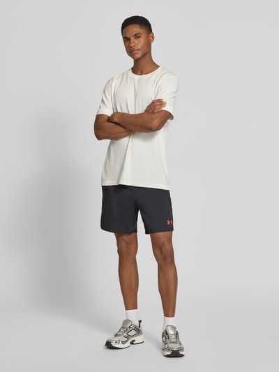 Mężczyznamodel nosi szorty z logo i wpuszczanymi kieszeniami od Under Armour, krój regular fit, elastyczny pas, szerokość w rozmiarze M: 38 cm, ciemny kolor z kontrastowym logo, cała sylwetka z przodu.