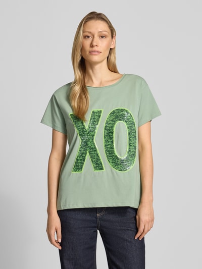 Vrouwenmodel draagt T-shirt met Paillettenbesatz van miss goodlife in lichtgroen met grote glanzende letters, rechte fit, ronde hals, katoen-elastaanmix, ruglengte maat S 62 cm. Vooraanzicht bovenlichaam.