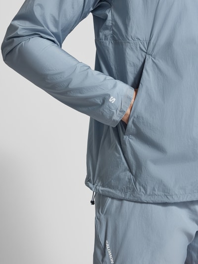 Männermodel trägt Jacke mit Logo und Eingrifftaschen von Salomon in Hellblau, Regular-Fit, Reißverschluss, Nahaufnahme Oberkörper. Rückenlänge 70 cm, Schulterbreite 43 cm, Brustweite 35 cm, Ärmellänge 67 cm.