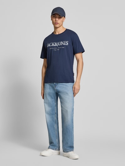 Mannelijk model draagt T-shirt uit katoen model 'DEVIN' van Jack & Jones, recht model, ronde hals, labelprint, ruglengte bij maat M 65 cm, volledig lichaam van voren.
