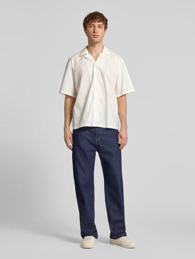 Männermodel trägt Relaxed Fit Freizeithemd aus reiner Baumwolle Modell 'Eligino' von HUGO in Optik: Unifarben, Passform: Relaxed-Fit, Hemdkragen, einreihige Knopfleiste, Muster: Gestreift, Rückenpasse, Verschluss: Knopfleiste, Ärmelform: Kurzarm, Materialverarbeitung: Popeline, reiner Baumwolle, natürliche Struktur, cremefarbene Töne, Ganzkörperansicht von vorne.