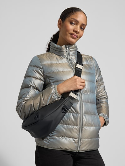 Frauenmodel trägt Handtasche mit verstellbarem Schulterriemen Modell 'Valeria' von RAINS, schwarzes Material, metallische Optik der Jacke, Hauptfach mit Reißverschluss, Ganzkörperansicht von vorne.