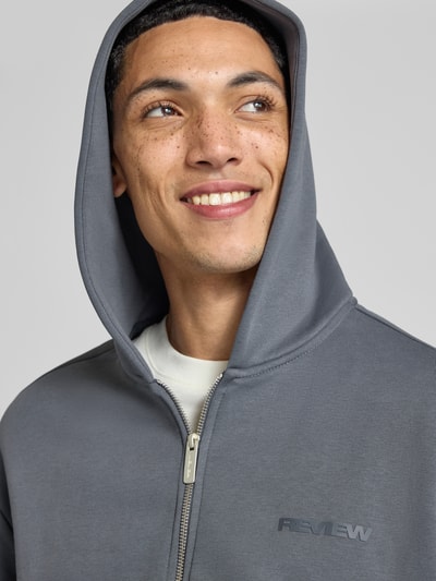 Männermodel trägt Relaxed Fit Sweatjacke aus Baumwoll-Mix mit Label-Detail von REVIEW in Grau, weiche Textur, Nahaufnahme Oberkörper.