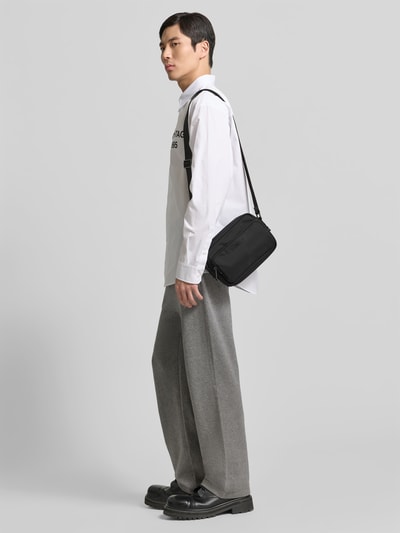 Männermodel trägt schwarze Crossbody Bag mit Label-Detail von Dsquared2, Reißverschlussfächer, Schulterriemen, Ganzkörperansicht von der Seite