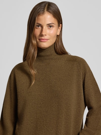 Frauenmodel trägt Strickpullover mit Stehkragen Modell 'LYZIMA' von DRYKORN aus reiner Baumwolle in Oliv, Nahaufnahme Oberkörper.