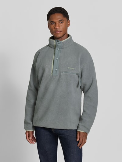 Męski model ma na sobie Fleecepullover mit Label-Patch Model 'Helvetia™ II' od Columbia, prosty krój, stójka, listwa z guzikami, naszywka z logo, kieszeń na piersi z zamkiem błyskawicznym, długość tyłu w rozmiarze M: 70 cm, długość rękawów: 62 cm, widok całej sylwetki z przodu.