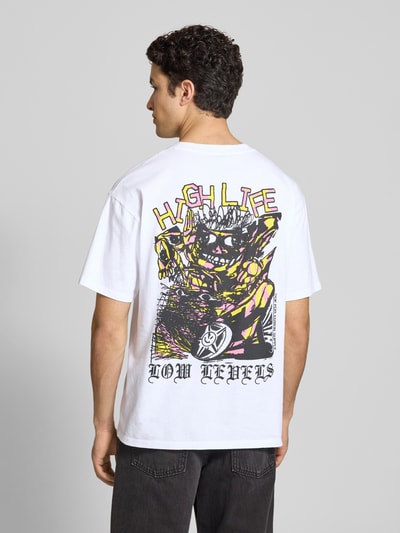 Męskimodel nosi białe męski t-shirt z nadrukiem model 'HATTY MAN' od Edwin z bawełny, krój relaxed fit, okrągły dekolt, długość tyłu w rozmiarze M: 73 cm, całkowity widok z tyłu.