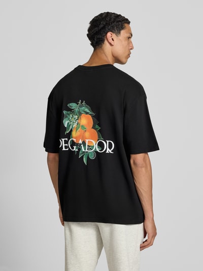 Männermodel trägt oversized fit heren T-shirt van puur katoen, model 'Viborg' van Pegador met logoprint en print aan de achterkant. Ganzkörperansicht Rückansicht.