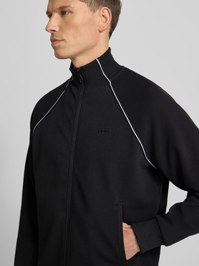 Männermodel draagt Regular Fit Sweat-Anzug aus Baumwoll-Mix Modell 'TRACKSUIT SET' van BOSS Green in effen zwart met witte paspels, staande kraag en geribde boorden, Nahaufnahme Oberkörper.