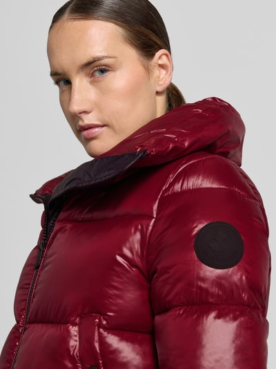 Frauenmodel trägt Regular Fit Steppjacke mit Stehkragen Modell 'Isla' von Save The Duck in glänzendem Dunkelrot, Nahaufnahme Oberkörper.