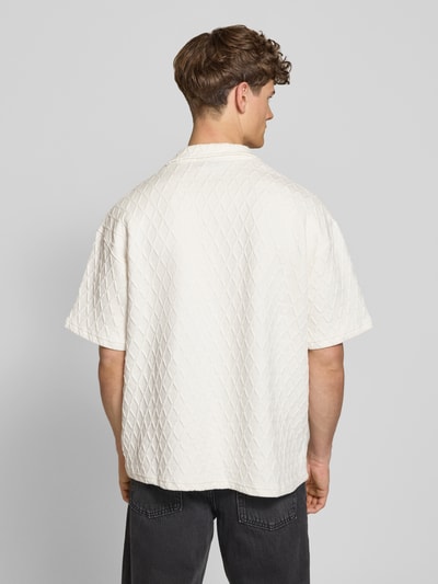 Männermodel trägt Regular Fit Freizeithemd mit Label-Stitching Modell 'Jovren' von Pegador in Creme, Elastischer-Material-Mix, Rückansicht Ganzkörperansicht. Rückenlänge bei Größe M: 72 cm, Schulterbreite: 45 cm, Ärmellänge: 33 cm, Halbarm, Reverskragen, Knopfleiste, Struktur mit Rautenmuster.