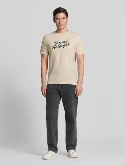 Männermodel trägt Regular Fit T-Shirt aus reiner Baumwolle von Tommy Hilfiger in Beige mit Label Print, unifarben, Ganzkörperansicht von vorne.