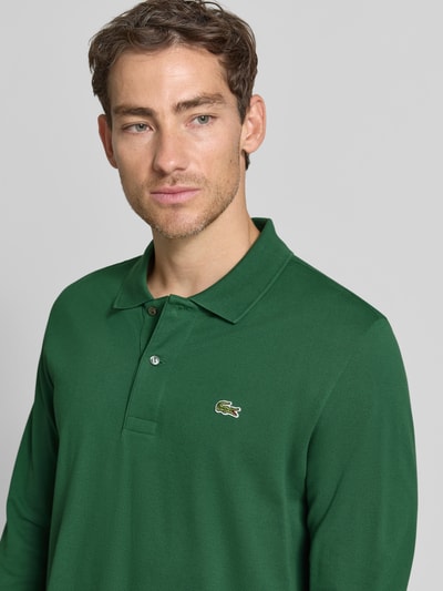 Männermodel trägt Regular Fit Poloshirt aus reiner Baumwolle von Lacoste in Dunkelgrün, glatte Struktur, Nahaufnahme Oberkörper, Herren Poloshirt von Lacoste.