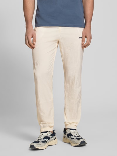 Männermodel trägt cremefarbene Straight Fit Stoffhose mit Logo-Stitching Modell 'Nayla' von SERGIO TACCHINI, elastischer Bund, Vorderansicht Ganzkörperansicht.
