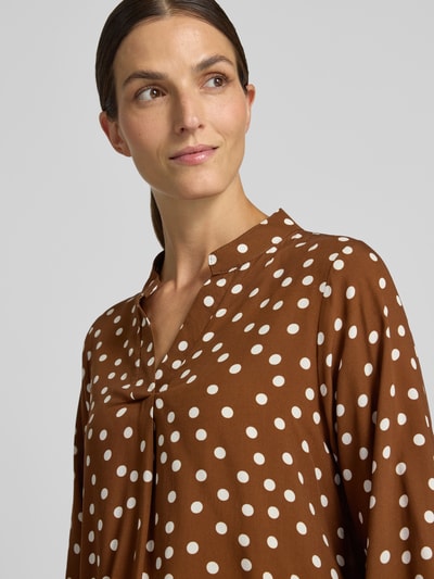 Frauenmodel trägt Relaxed Fit Bluse aus reiner Viskose-Mix Modell 'Valeria' von ZABAIONE mit weißen Punkten auf braunem Stoff, Nahaufnahme Oberkörper, Serafino Ausschnitt, langärmelig, Rückenlänge bei Größe S 54 cm, Ärmellänge 58 cm.