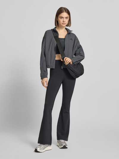 Frauenmodel trägt schwarze Flared Fit Stoffhose mit breitem Bund Modell 'All Me' von adidas Sportswear, elastischer Material-Mix, Ganzkörperansicht von vorne.
