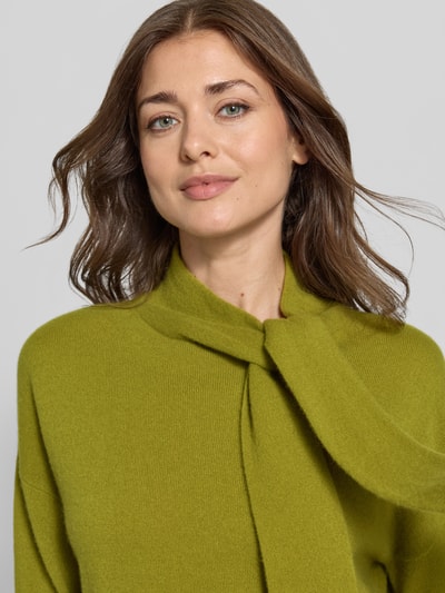 Vrouwenmodel draagt pullover van kasjmier met sjaal-detail van Christian Berg Woman in groen, recht model, opstaande kraag, geribde boorden, oversneden schouders, pure kasjmier, ruglengte maat M 60 cm, mouwlengte maat M 54 cm, detailopname bovenlichaam.